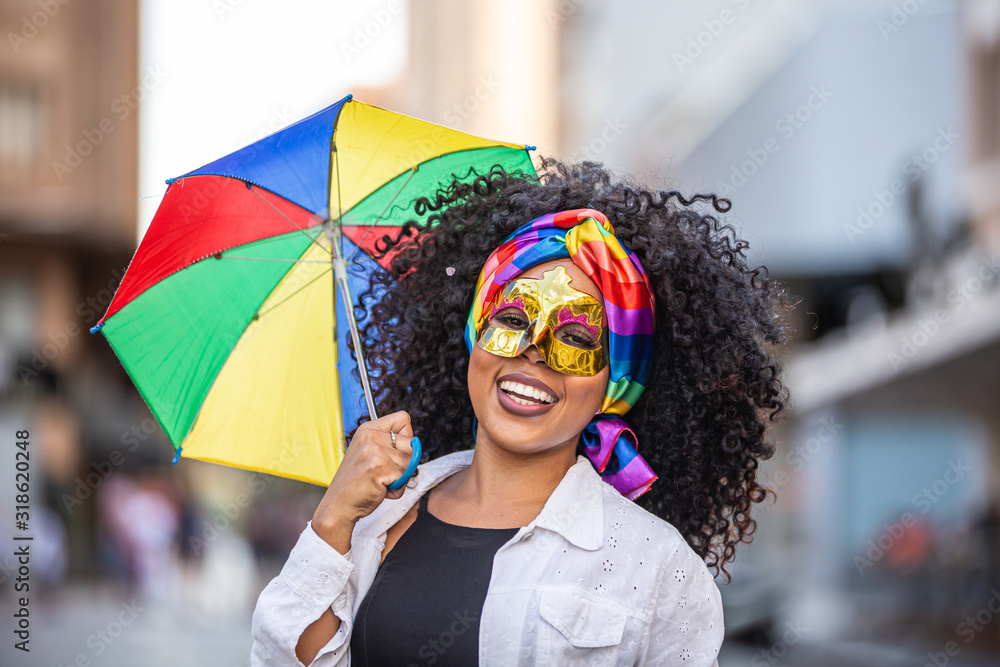 Young curly hair woman celebrating the Brazilian carnival party with Frevo umbrella on street. - obrazy, fototapety, plakaty 