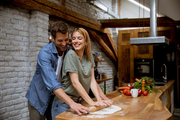 Wall Mural - Lovely cheerful young couple preparing dinner together and having fun at rustic kitchen