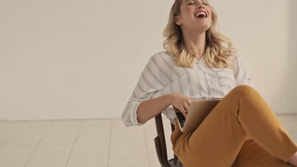 Poster - Good-looking smiling young woman is laughing while using her laptop in white office