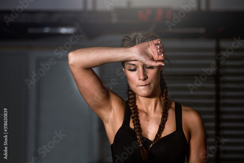 Young sweaty beautiful muscular fit girl sweep sweat from her forehead with her hand after heavy hardcore crossfit workout training in the gym