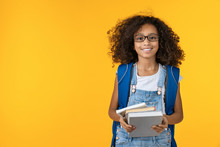 Cheerful Young African Girl Kid In Eyeglasses Holding Notebook And Books For Study Isolated Over Yellow Background