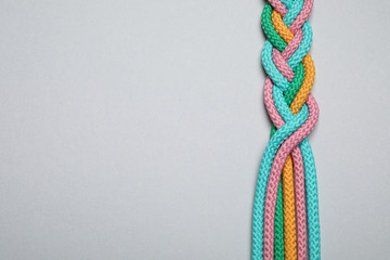 Wall Mural - Top view of braided colorful ropes on light grey background, space for text. Unity concept