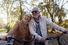 Cheerful Active Senior Couple With Bicycle In Public Park Together Having Fun. Perfect Activities For Elderly People.