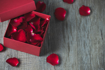 Red gift box With rose petals inside, placed on a gray wooden floor, top view and copy space, valentine's day theme