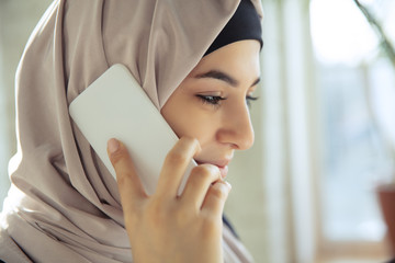 Wall Mural - Talking on phone, smiling. Close up portrait of a beautiful arabian businesswoman wearing hijab while working at openspace or office. Concept of occupation, leadership, success, modern solution.