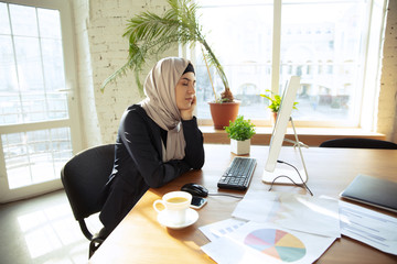 Wall Mural - Portrait of a beautiful arabian businesswoman wearing hijab while working at openspace or office. Concept of occupation, freedom in business area, leadership, success, modern solution.