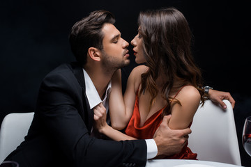 Wall Mural - Side view of elegant couple looking at each other during romantic dinner isolated on black