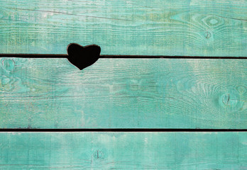 a hole in the shape of a heart in a wooden wall made of old boards painted blue. Texture background for Valentine's day use, horizontal orientation