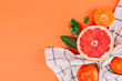 Fresh ripe mandarin and grapefruit with green leaves on white towel on orange background.