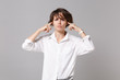 © ViDi Studio - Dissatisfied young business woman in white shirt posing isolated on grey wall background studio portrait. Achievement career wealth business concept. Mock up copy space. Covering ears with fingers.