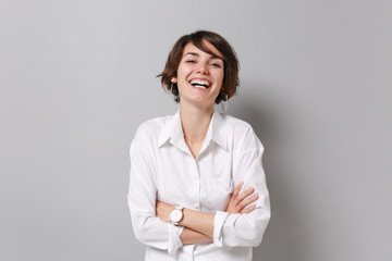 Wall Mural - Laughing young business woman in white shirt posing isolated on grey background studio portrait. Achievement career wealth business concept. Mock up copy space. Holding hands crossed, looking camera.