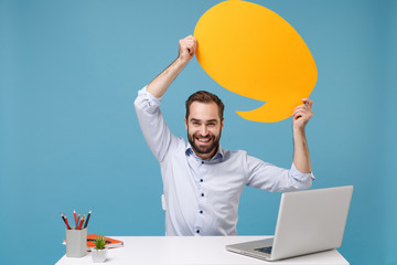 Canvas Print - Smiling young man in shirt sit work at desk with pc laptop isolated on pastel blue background. Achievement business career concept. Mock up copy space. Hold yellow empty blank Say cloud speech bubble.