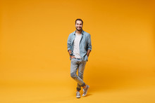 Smiling Young Bearded Man In Casual Blue Shirt Posing Isolated On Yellow Orange Background, Studio Portrait. People Sincere Emotions Lifestyle Concept. Mock Up Copy Space. Holding Hands In Pockets.