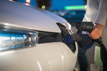 Young woman charging an electric vehicle. Car sharing concept.