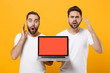 © ViDi Studio - Shocked young men guys friends in white t-shirts isolated on yellow orange background. People lifestyle concept. Mock up copy space. Holding laptop pc computer with blank empty screen spreading hands.