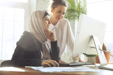 Wall Mural - Discussion with colleague. Beautiful arabian businesswoman wearing hijab while working at openspace or office. Concept of occupation, freedom in business area, leadership, success, modern solution.