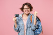 © ViDi Studio - Happy young woman student in denim clothes glasses backpack posing isolated on pastel pink background. Education in high school university college concept. Doing winner gesture, hold credit bank card.