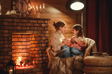 family mother and child reading book and drink tea on winter evening by fireplace