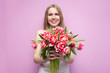 © Богдан Маліцький - young beautiful girl holds a bouquet of flowers on a pink background, close-up of a bouquet of tulips