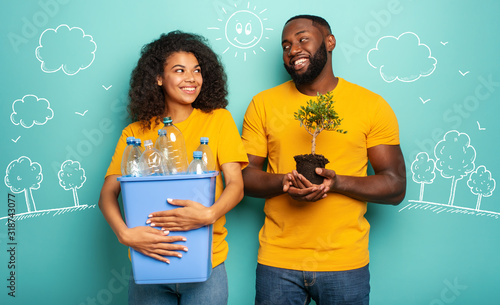 Cuadros en Lienzo Happy couple hold a plastic container with bottles and a small tree over a light blue color