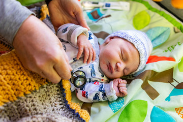 Wall Mural - A close up shot on the hands of family doctor checking health of cute baby boy wearing tractor patterned romper suit, listening for healthy heart beat