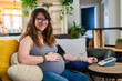 © Valmedia - Happy portrait of a young woman in later stages of pregnancy carrying out routine health checks at home, wearing a blood pressure meter with arm cuff