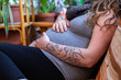 A close up shot of a heavily pregnant woman in the third trimester relaxing on sofa in family room, feeling movements and kicks with hands near labor