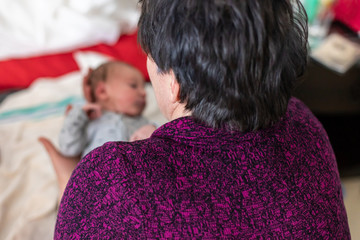 Wall Mural - A Grandmother is seen from the rear, picking up newborn baby for first time in delivery room, magical moment as family bond and celebrate new life