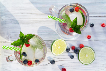 Wall Mural - Homemade cold summer cocktail with mineral water, ice cubes, mint, lime, berry juice and fresh berries in glasses with straws, top view