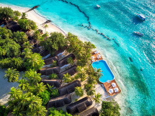 Aerial topdown view of tropical island  resort. Bungalows and pool on white sand beach. Turquoise clear water and corals. Summer on maldives