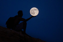 Optical Illusion Of Man Holding Full Moon In Clear Blue Sky