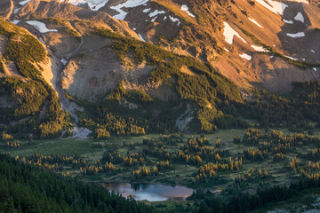 Wall Mural - the last rays of sunset work their way up a steep mountain slope as the lake filled green valley bel