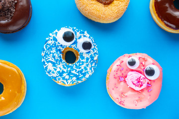 Wall Mural - A blue donut with a pink donut with funny faces on a blue background looking each other