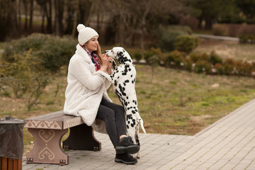 Wall Mural - A beautiful, fashionable girl in an artificial white fur coat with her dog Dalmatian play, make friends on a walk. Concept: love between owner and dog. Protection of animals.