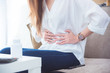 A woman having stomachache sitting on sofa and holding her belly by hands.