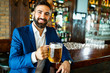 © NDABCREATIVITY - Happy businessman raising glass of beer after work in a pub