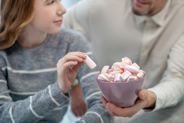 Long-haired girl in grey shirt taking marshmallow