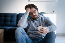 Portrait Of Worried Guy Holding Cellphone At Home
