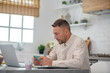 © zinkevych - Good-looking bearded man sitting in the kitchen and typing a message