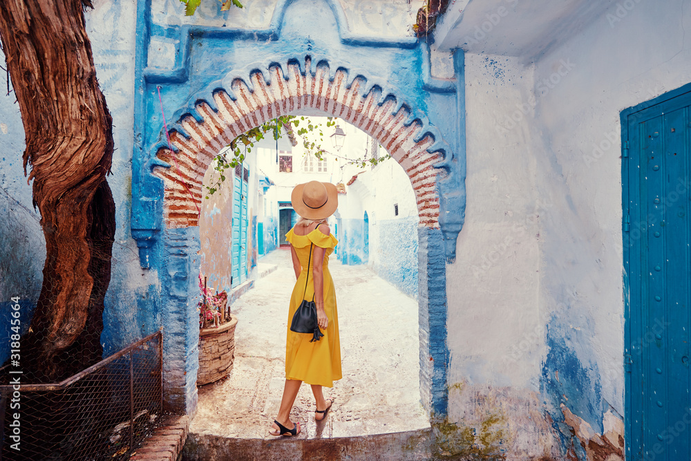 Colorful traveling by Morocco. Young woman in yellow dress walking in  medina of  blue city Chefchaouen. - obrazy, fototapety, plakaty 