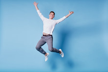 Colorful Studio Portrait Of Happy Young Man Jumping Against Blue Background.
