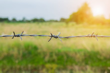Close-Up Of Barbed Wire Fence Over Field