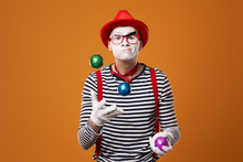 Mime Man In Vest And Red Hat Juggles With Colorful Balls On Orange Background