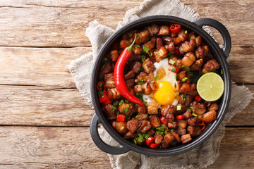 Tasty filipino sisig food served with egg, lime and chili pepper close-up in a pan. Horizontal top view