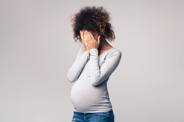 Depression during pregnancy. Afro woman covering face with hands