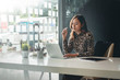 © amnaj - Young asian businesswoman sitting on her workplace in the office. Young woman working at laptop in the office.