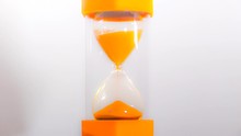Close POV Timelapse Shot Of A Bright Orange Glass Timer In Action, With Orange Sand Flowing And Forming A Heap At The Bottom.
