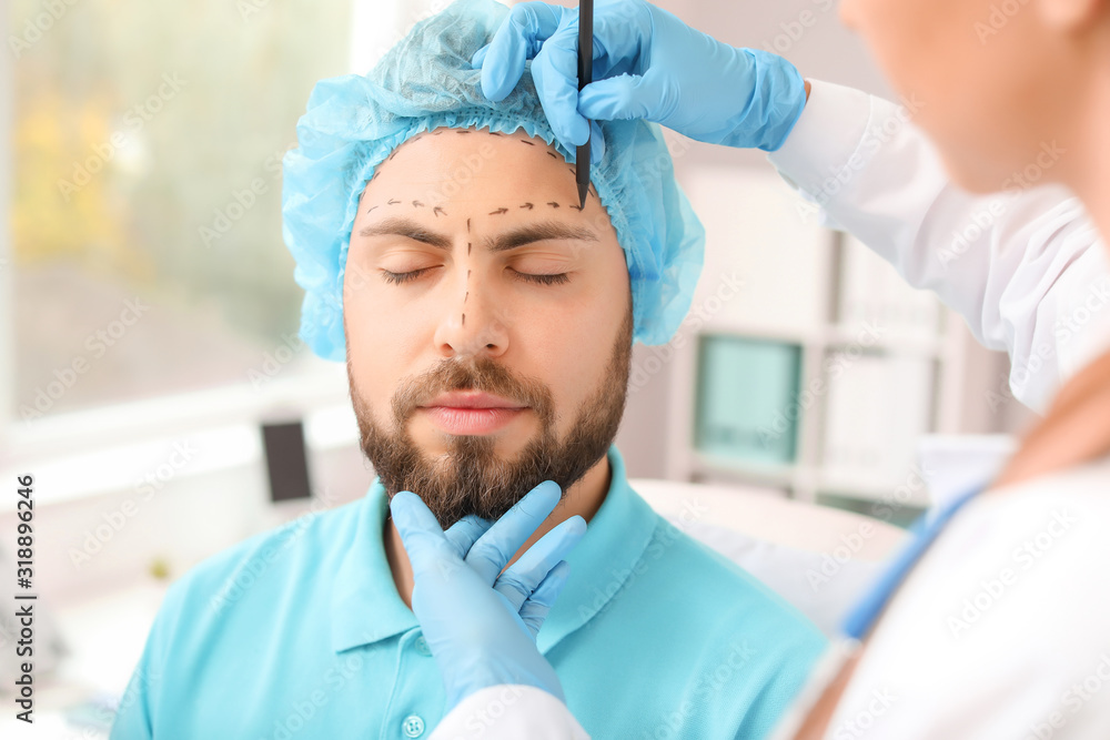 Plastic surgeon applying marks on patient's face in clinic