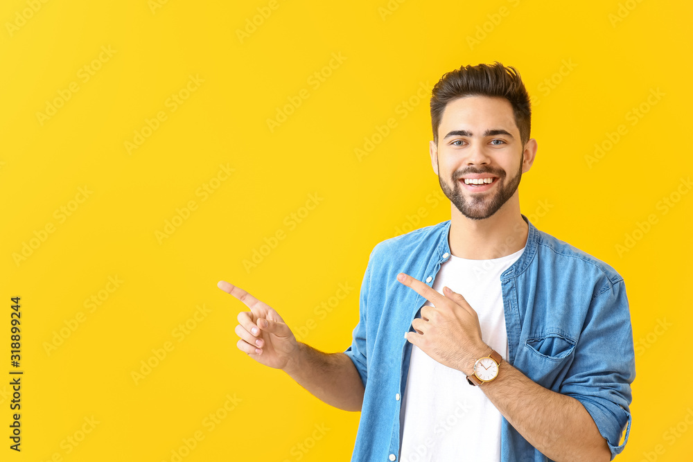 Handsome young man pointing at something on color background - obrazy, fototapety, plakaty 