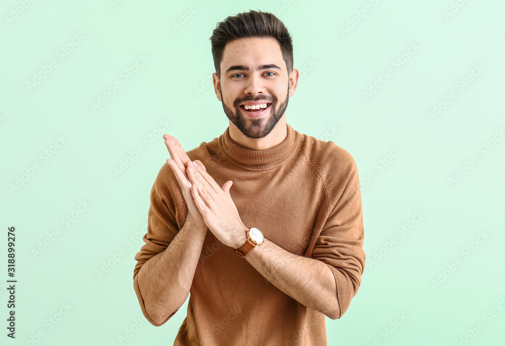 Handsome young man rubbing his hands on color background